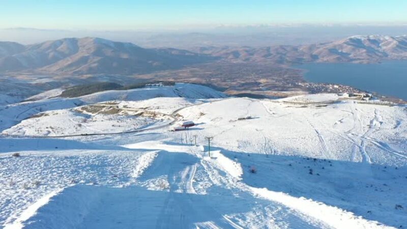 Elazığ’ın Sivrice ilçesindeki göl manzaralı Hazarbaba Kayak Merkezi'nde son haftalarda etkili olan kar, yeni sezon için kayakseverleri umutlandırdı. Hazarbaba Kayak Merkezi’nde Kar Var mı? Hazarbaba Kayak Merkezi’nde kar var.  Geçen sezon yeterli miktarda kar alamaması nedeniyle sezonu açamayan kayak merkezinde kasım sonu itibarıyla etkili olan yağışla, kar kalınlığı ortalama 30 santimetreye ulaştı. "Doğu'nun saklı denizi" olarak adlandırılan Hazar Gölü manzarasıyla da ilgi gören kayak merkezinde yeni sezon için yürütülen bakım ve yenileme çalışmaları tamamlanma noktasına gelirken, sezonun açılabilmesi için 15-20 santimetre daha kar bekleniyor. Hazarbaba Dağı'nın eteklerinde 2 bin 300 rakımda yer alan kayak merkezi, 1300 metrelik dikey ve 6 kilometrelik yatay pist alanı ile ziyaretçilerine kızak, kayak, snowboard, kar motoru, göl manzaralı restoran ve kafeterya imkanlarıyla hizmet veriyor. - "Yeterli kar yağışıyla beraber sezonu açacağız" Hazarbaba Kayak Merkezi yetkilisi İsmet Berkay Altundaş, AA muhabirine, ziyaretçilere en iyi hizmeti sunmak adına sezon hazırlıklarını titizlikle yürüttüklerini, mevcut imkanları daha da geliştirdiklerini söyledi. Geçen haftalarda yağışla kar kalınlığının 25-30 santimetreye ulaştığını ifade eden Altundaş, "Özellikle zirve kısmında daha fazla kar kalınlığına ulaştık. Kayak sezonunu tam anlamıyla açabilmemiz adına 40 ila 50 santimetre arasında kar kalınlığına ihtiyacımız var. Önümüzdeki günlerde yoğun kar yağışı bekliyoruz." dedi. Sezon öncesinde gerekli bakım çalışmalarını yaptıklarını, tesiste eksikliğin bulunmadığını kaydeden Altundaş, "Tek eksiğimiz kar. Umarım ilerleyen günlerde yeterli kar yağışıyla beraber sezonu açacağız." ifadesini kullandı. Altundaş, bu yıl erken yağan karla son 10 senenin en uzun kayak sezonunu geçirmeyi umduklarını dile getirerek, şöyle devam etti: "Yeni sezonda ziyaretçilerimiz için üç noktada hizmet veriyoruz. Bir noktamızda kayak ekipmanları kiralama ve sıcak içecek satışımız mevcut. Bir üst istasyonumuzda, sucuk ekmek, köfte ekmek, sıcak içecekler, meşrubatlar gibi yiyecek ve içecek hizmetimiz var. En üst istasyonumuzda, bu yıl yenilediğimiz, 250 metrekareye yakın büyütme yaptığımız hem günübirlik tesis hem de 12 ay hizmet verecek alakart restoranımızı faaliyete alıyoruz. İnşallah yılbaşından önce açılışını yapacağız. Ziyaretçilerimize cam konseptli, göl manzarasını kesintisiz izleyebilecekleri bir yer sunuyoruz." - "En büyük özelliği iki göl manzarası olması" Altundaş, merkezde profesyonel, acemi, macera ve baby-lift olmak üzere 4 pist ve teleski bulunduğunu bildirdi. Merkezde ziyaretçilerin eşsiz manzara eşliğinde kayak yapmanın keyfini çıkardığını anlatan Altundaş, şunları kaydetti: "Hazarbaba Kayak Merkezi'ni diğerlerinden ayıran en büyük özelliği, iki göl manzarası olması. İlk aşamada Hazar Gölü, onun arkasında Keban Baraj Gölü manzarasını seyredebiliyorsunuz. Hava sisli olmadığı takdirde, kayakseverler kayarken iki gölü de görebilme şansına sahip. Ayrıca buradaki kristal kar özelliği, kayak tutkunlarının yine vazgeçilmezi. Geniş bir pist alanımız var. Tüm ziyaretçilerimizi kar keyfi için bekliyoruz." Altundaş, karla kaplı merkezde ziyaretçiler için kızak hizmeti de vermeye başladıklarını sözlerine ekledi.